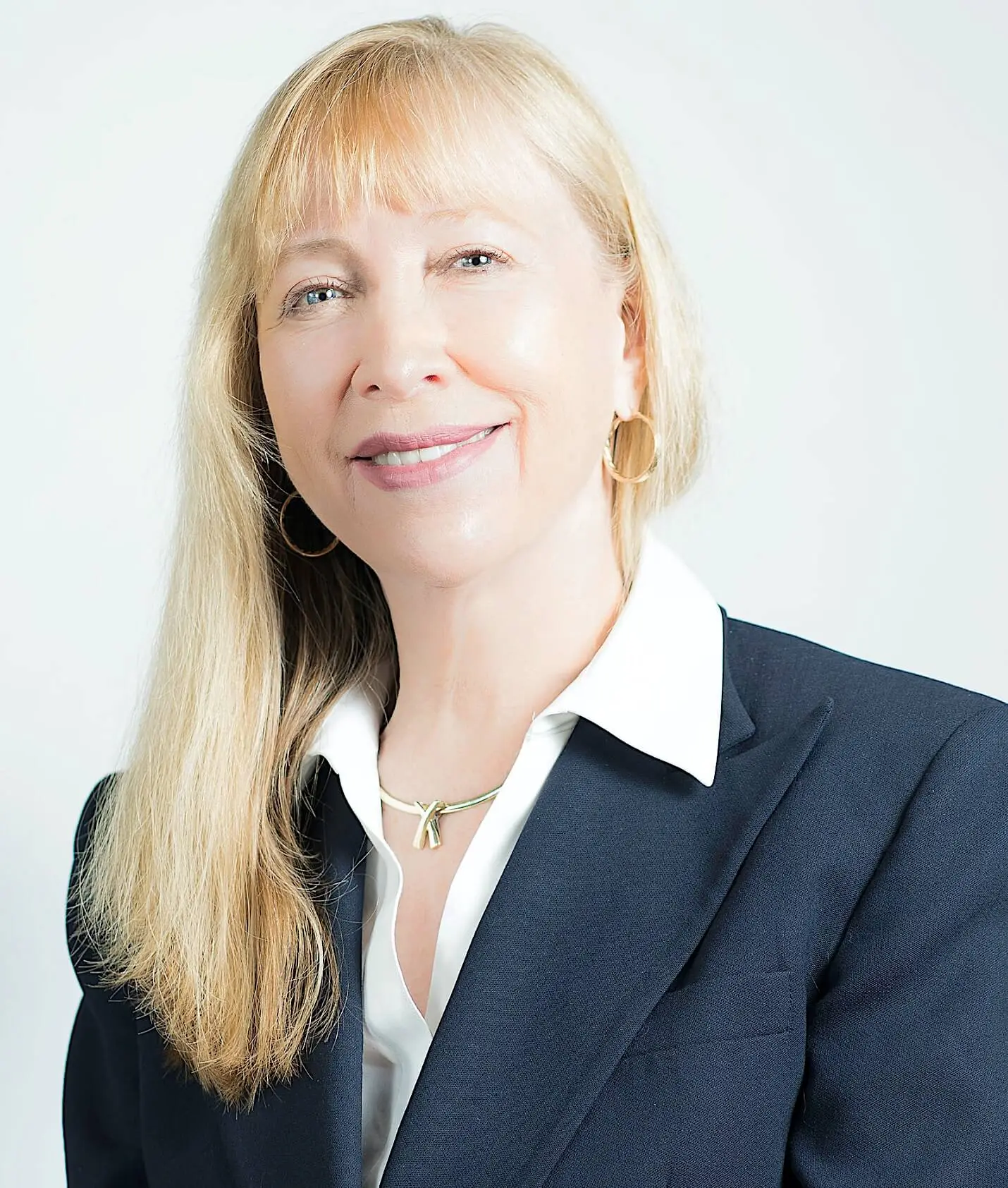 Professional headshot of a woman with long blonde hair, wearing a dark blazer over a white shirt. She is smiling confidently against a light background. This image conveys professionalism and approachability, suitable for business or corporate contexts.